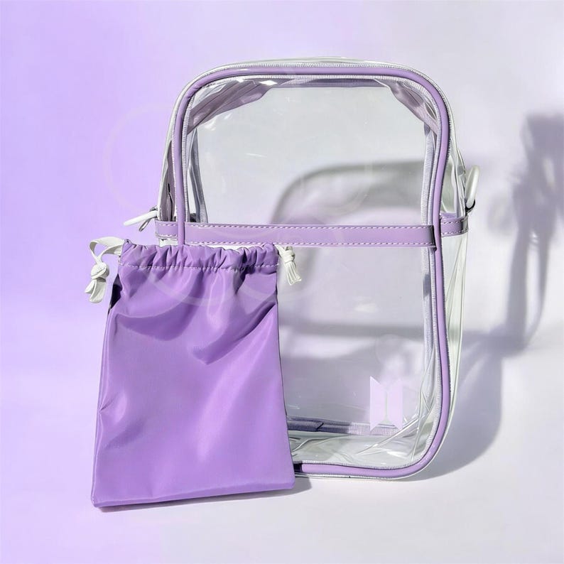 Peut inclure: Un sac transparent rectangulaire avec une bordure violette et une pochette assortie &agrave; cordon de serrage. Le sac a une poign&eacute;e blanche et une fermeture &eacute;clair argent&eacute;e. La pochette est de couleur violette unie. Le sac mesure environ 25 cm de haut et 20 cm de large.