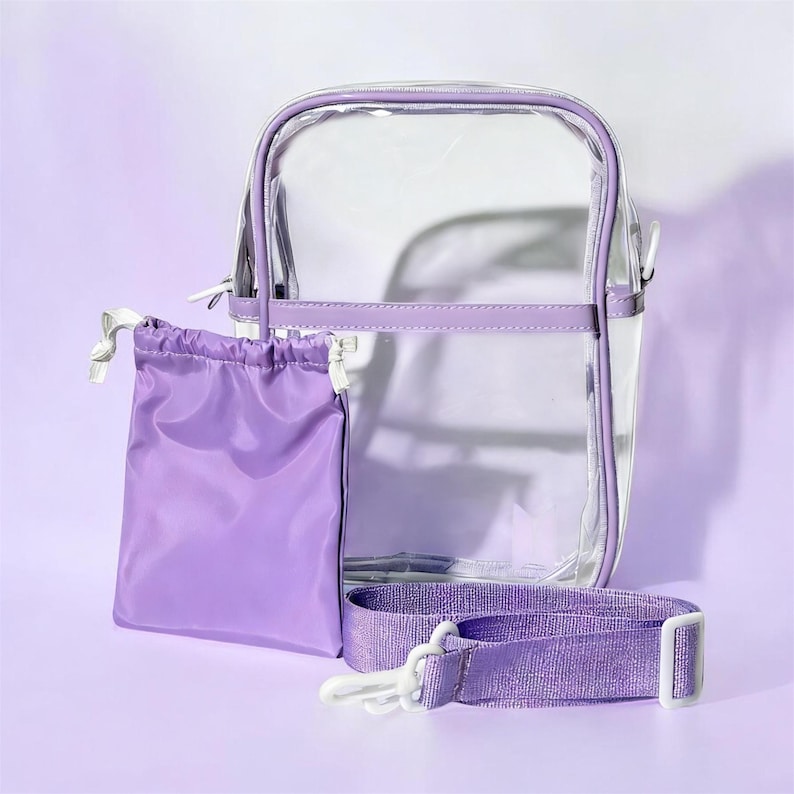 Peut inclure: Un sac bandouli&egrave;re transparent avec une bordure, une sangle et une pochette assortie &agrave; cordon de serrage de couleur violette. Le sac a une forme rectangulaire avec une fermeture &eacute;clair. La sangle r&eacute;glable est fix&eacute;e avec des clips en plastique blancs.