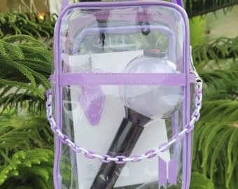 May include: A clear, rectangular shoulder bag with light purple trim and a matching chain strap. Inside, a white card with the Chinese character 承 and a BTS logo is visible, along with a spherical light stick featuring a black handle and clear dome.