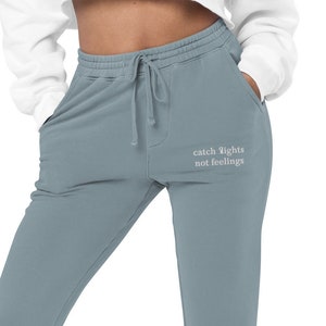 May include: A pair of light blue sweatpants with a white drawstring and the text "catch flights not feelings" embroidered on the right leg.