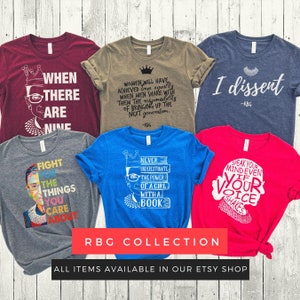May include: A collection of six t-shirts featuring quotes and illustrations of Ruth Bader Ginsburg. The shirts are in various colors, including red, blue, green, and gray. The text on the shirts includes quotes such as "When there are nine", "I dissent", "Never underestimate the power of a girl with a book", and "Fight for the things you care about".