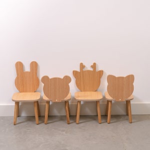 May include: Four wooden children's chairs with animal-shaped backs. The chairs are in a row, from left to right: a bunny, a bear, a deer, and a cat. The chairs are all made of natural wood and have a simple, minimalist design.