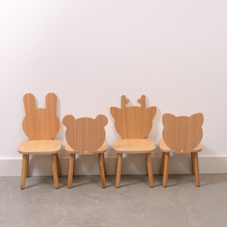 May include: Four wooden children's chairs with animal-shaped backs. The chairs are in a row, from left to right: a bunny, a bear, a deer, and a cat. The chairs are all made of natural wood and have a simple, minimalist design.