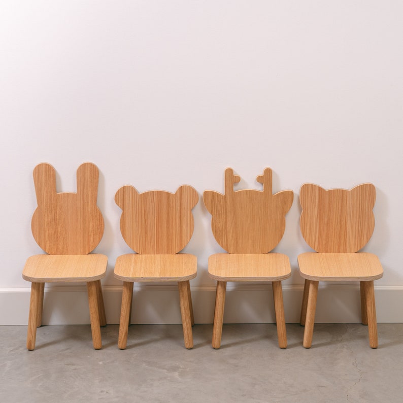 May include: Four wooden children's chairs with animal-shaped backs. The chairs are in a row, from left to right: a bunny, a bear, a reindeer, and a bear. The chairs are all made of natural wood and have a simple, minimalist design.