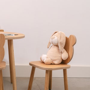 May include: A wooden children's chair with a plush bunny toy sitting on the seat. The chair has a rounded back and four legs.