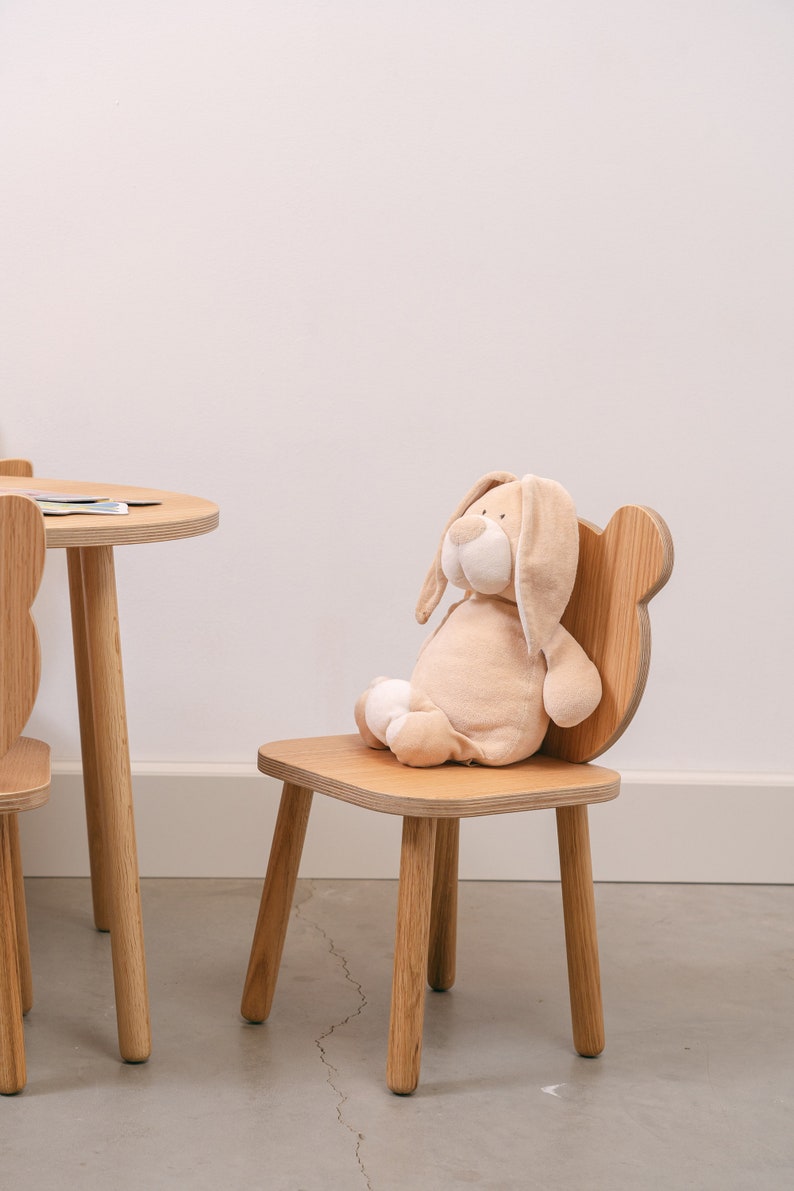 May include: A wooden children's chair with a plush bunny toy sitting on the seat. The chair has a rounded back and four legs.