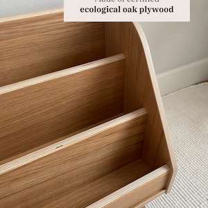 Puede incluir: Una estanter&iacute;a de madera con tres estantes, hecha de madera contrachapada de roble ecol&oacute;gico certificada. Los estantes son curvos en la parte superior y tienen un acabado de madera natural.