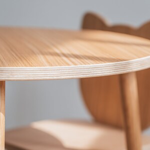 May include: A close-up of a light wood children's table and chair set. The table is round and has a white edge. The chair has a unique animal-shaped back.