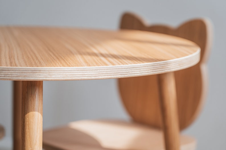 May include: A close-up of a light wood children's table and chair set. The table is round and has a white edge. The chair has a unique animal-shaped back.