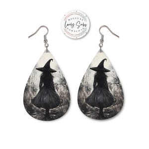 May include: A pair of teardrop-shaped earrings featuring a witch silhouette in a black dress and hat, set against a grayscale forest scene. The earrings have silver hooks and are designed with a gothic or Halloween theme.