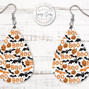 May include: Teardrop-shaped Halloween earrings with a white background, featuring orange pumpkins, bats, and the word "BOO" in orange. The earrings have silver-colored fish hook ear wires.