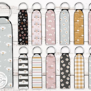 May include: Set of 12 keychains featuring various patterns, including floral, striped, and checkered designs. The keychains are made of fabric and have a black trim. Some keychains feature the text "hello daisy".