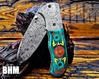 May include: A folding pocket knife with a patterned steel blade and a turquoise handle with red and yellow accents. The handle has a dragon design and the text "BHM" is visible on the blade.