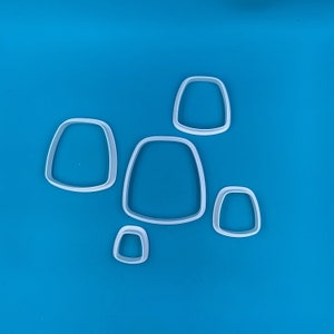 Peut inclure: Cinq emporte-pièces en plastique blanc de différentes tailles et formes, sur un fond bleu. Les emporte-pièces ont la forme de rectangles arrondis.
