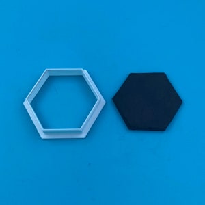 May include: A white plastic hexagon cookie cutter and a black hexagon-shaped piece of fondant.