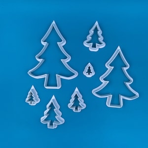 May include: A set of seven white plastic Christmas tree cookie cutters of varying sizes on a blue background.