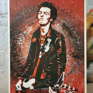 Op de afbeelding: Een zwart-wit zeefdruk van een muzikant die basgitaar speelt. De achtergrond is rood met witte en grijze krabbels. De print is gesigneerd "Rich 69 Sig" en genummerd "404/500".