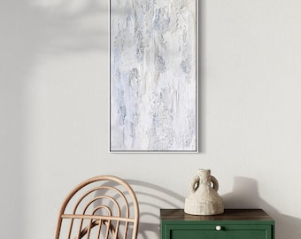 Può includere: Opera d'arte astratta e strutturata in una cornice rettangolare nera. L'opera presenta una palette di colori bianca e azzurra con una texture in rilievo e stratificata. È esposta su una parete bianca, sopra un mobile verde e una sedia di legno.