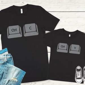 May include: Two black t-shirts with a computer keyboard key design. The larger shirt has the keys "Ctrl" and "C" printed on it. The smaller shirt has the keys "Ctrl" and "V" printed on it.