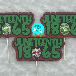 Puede incluir: Tres carteles de papel rojo y verde con el texto "Juneteenth 1865" en cada uno. Cada cartel tiene una piruleta unida en la parte inferior.