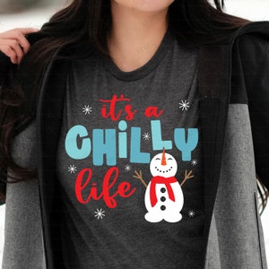 Puede incluir: Una camiseta gris oscuro con un gráfico de muñeco de nieve blanco y el texto "it's a chilly life" en letras rojas y azules.