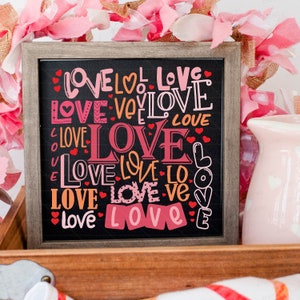 May include: A wooden framed chalkboard sign with the word "LOVE" repeated in various colors, fonts, and sizes. The sign is decorated with small red hearts.