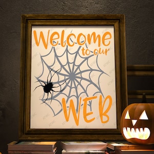 Könnte beinhalten: Ein gerahmtes Halloween-Schild mit einem Spinnennetz und einer Spinne darauf. Das Schild sagt "Willkommen in unserem Netz" in orangefarbenen Buchstaben.