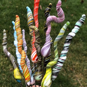 May include: A collection of colorful glass art pieces, each with a unique swirl pattern. The pieces are made of glass and have a variety of colors, including red, orange, yellow, green, blue, purple, and black.