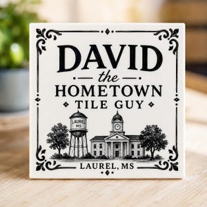 May include: A square white ceramic tile featuring black decorative borders and text that reads DAVID the HOMETOWN TILE GUY. Below the text is a black and white illustration of a water tower labeled LAUREL MS, a building with a clock tower, and trees.
