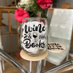 Könnte beinhalten: Ein klares Weinglas aus Glas mit einem schwarzen Vinyl-Aufkleber, auf dem "Wine & Books" mit einem Grafikmotiv von einem Weinglas und einem Stapel Büchern steht. Das Glas steht auf einem Untersetzer aus Holz.