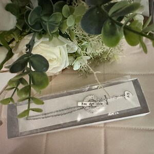 May include: A silver necklace with a charm that says "You got this" and a heart charm. The necklace is in a white box with a white background.