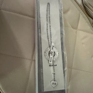 May include: Silver necklace with a heart charm that says "AD" and a round charm with the text "You got this" hanging from a silver chain. The necklace is in a white box.