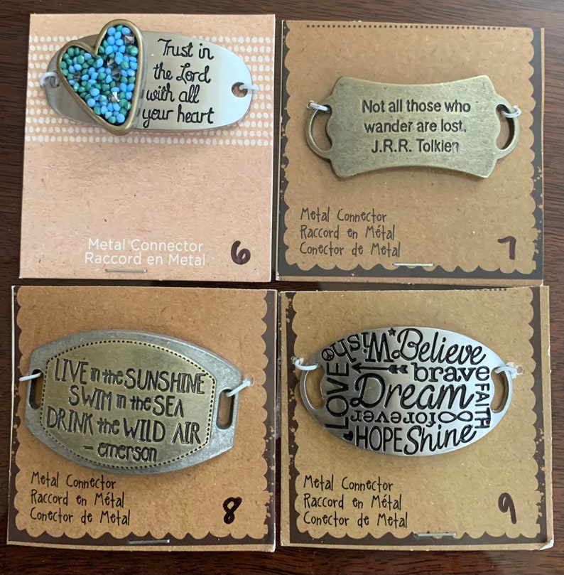 May include: Four metal charm tags with inspirational quotes and sayings. The charms are silver and gold in color and have a heart, a sun, and a star design. The charms are labeled with numbers 6, 7, 8, and 9.