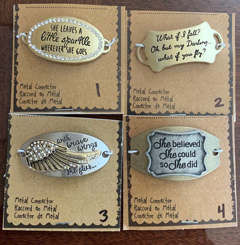 May include: Four metal charm bracelets with inspirational quotes. The charms are oval shaped and feature a gold or silver finish. The charms are numbered 1 through 4. The charms feature the following quotes: "She leaves a little sparkle wherever she goes", "What if I fall? Oh, but my Darling... what if you fly?", "With brave wings she flies...", and "She believed she could so she did".