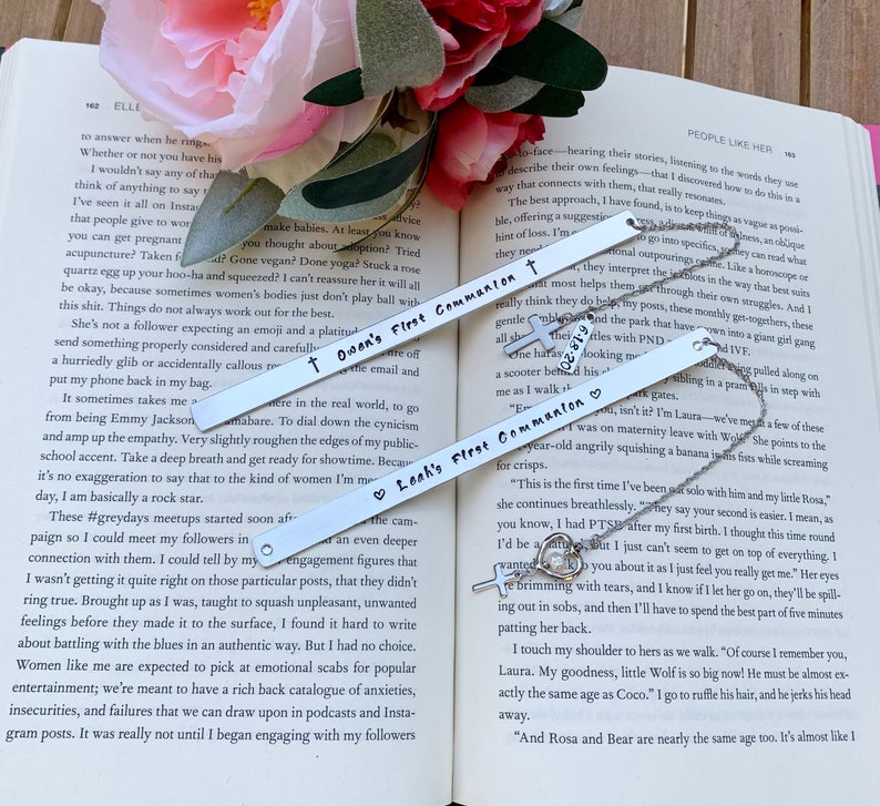 Pu&ograve; includere: Due segnalibri d'argento con un ciondolo a forma di croce. I segnalibri sono incisi con il testo "Leah's First Communion" e "Owen's First Communion".