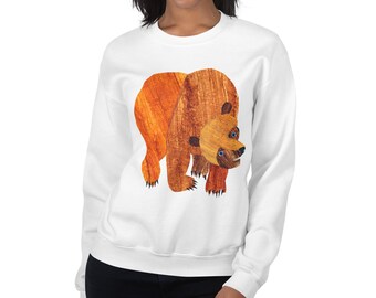 May include: White sweatshirt featuring a large illustration of a brown bear with orange and brown textured fur. The bear has blue eyes and black claws. The sweatshirt is a casual style.