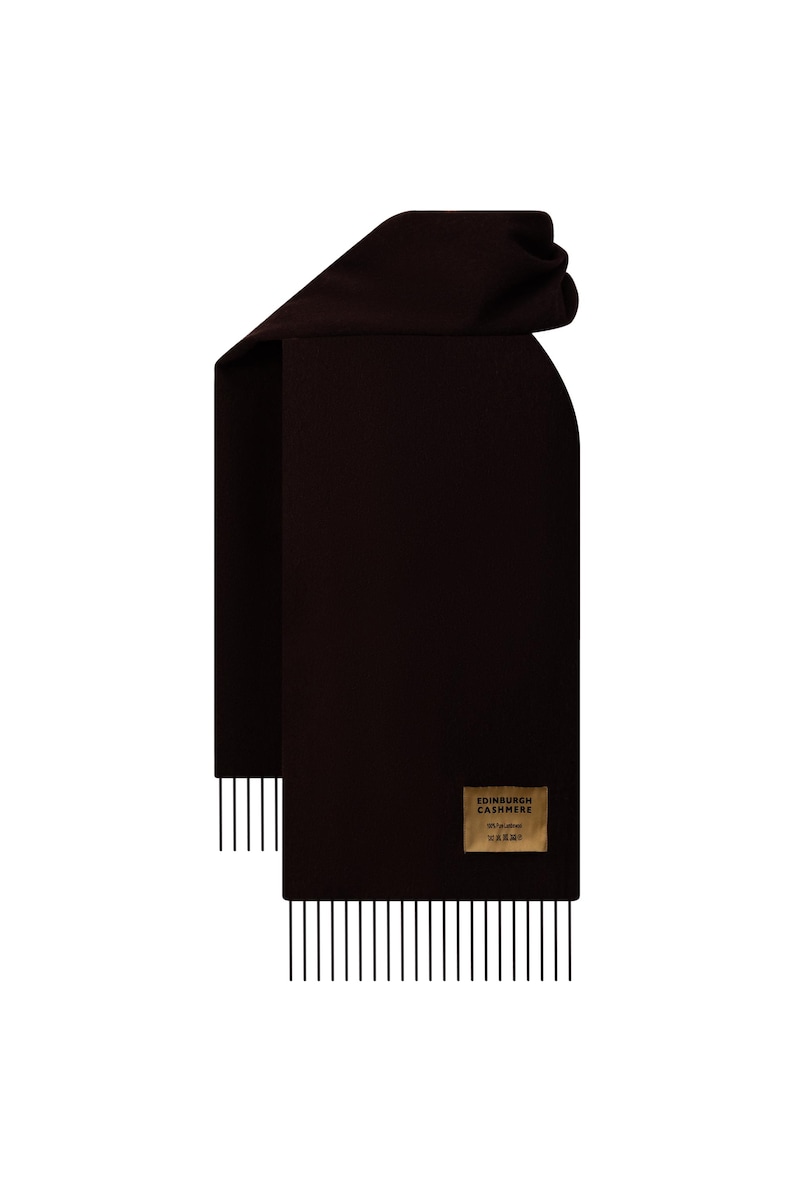 May include: A dark brown scarf with a rectangular shape and a fringed edge. The scarf has a label that reads "EDINBURGH CASHMERE". The scarf is made of a soft material.