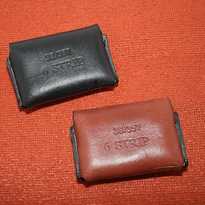 May include: Two leather cases for film, one black and one brown, with the text "38/357 6 STRIP" printed on each.