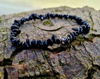May include: Black gemstone chip bracelet with a silver bead accent. The bracelet is on a rough, brown wooden surface.