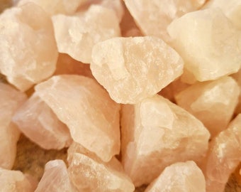 May include: A close-up of a pile of pink rose quartz crystals. The crystals are rough and have a natural, unpolished look.