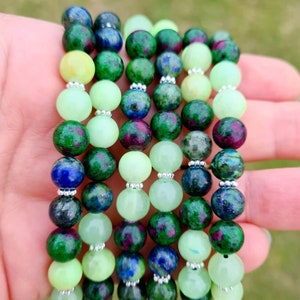 May include: A set of six bracelets made with green, blue, and white gemstone beads. The bracelets are stacked on top of each other and are being held in a hand.