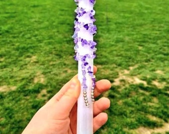 May include: A white selenite wand wrapped with amethyst crystals. The wand is about 10 inches long and is held in a hand.