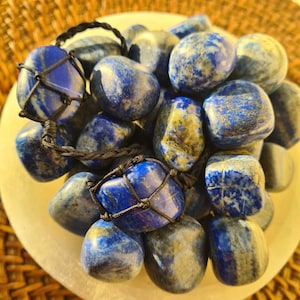 May include: A collection of tumbled lapis lazuli stones, some of which are tied together with black cord. The stones are a deep blue with gold flecks and have a smooth, polished finish.