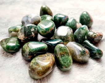 May include: A collection of green moss agate tumbled stones. The stones are smooth and polished, with a variety of green shades and patterns.