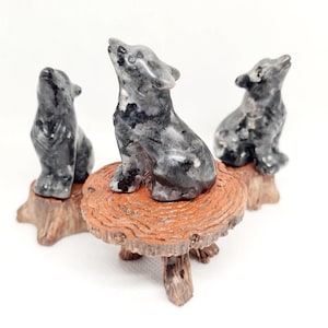 Könnte beinhalten: Drei schwarze und weiße Wolfsfiguren aus Stein, die auf einem Holzsockel sitzen. Die Wölfe heulen zum Mond.