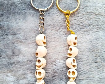 May include: Two skull keychain charms, one with a silver key ring and one with a gold key ring. Each charm features a chain of seven white skull beads.