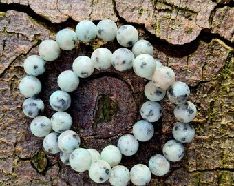 May include: A bracelet made of light green and white speckled beads. The bracelet is made of natural stone and is a beautiful and unique piece of jewelry.