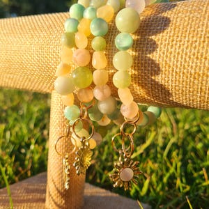 May include: Four beaded bracelets with green, yellow, and pink beads. The bracelets have gold charms in the shape of a sun.