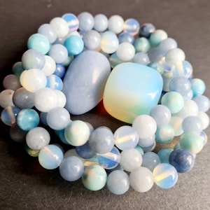 Könnte beinhalten: Eine Sammlung von blauen und weißen Edelsteinperlen, darunter Aquamarin, Opal und Lapislazuli. Die Perlen sind in einem kreisförmigen Muster angeordnet, mit einem größeren Opal-Stein in der Mitte.