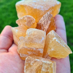 Può includere: Una collezione di cristalli di calcite grezzi e naturali in varie dimensioni e forme. I cristalli sono di colore giallo pallido e hanno un aspetto traslucido.